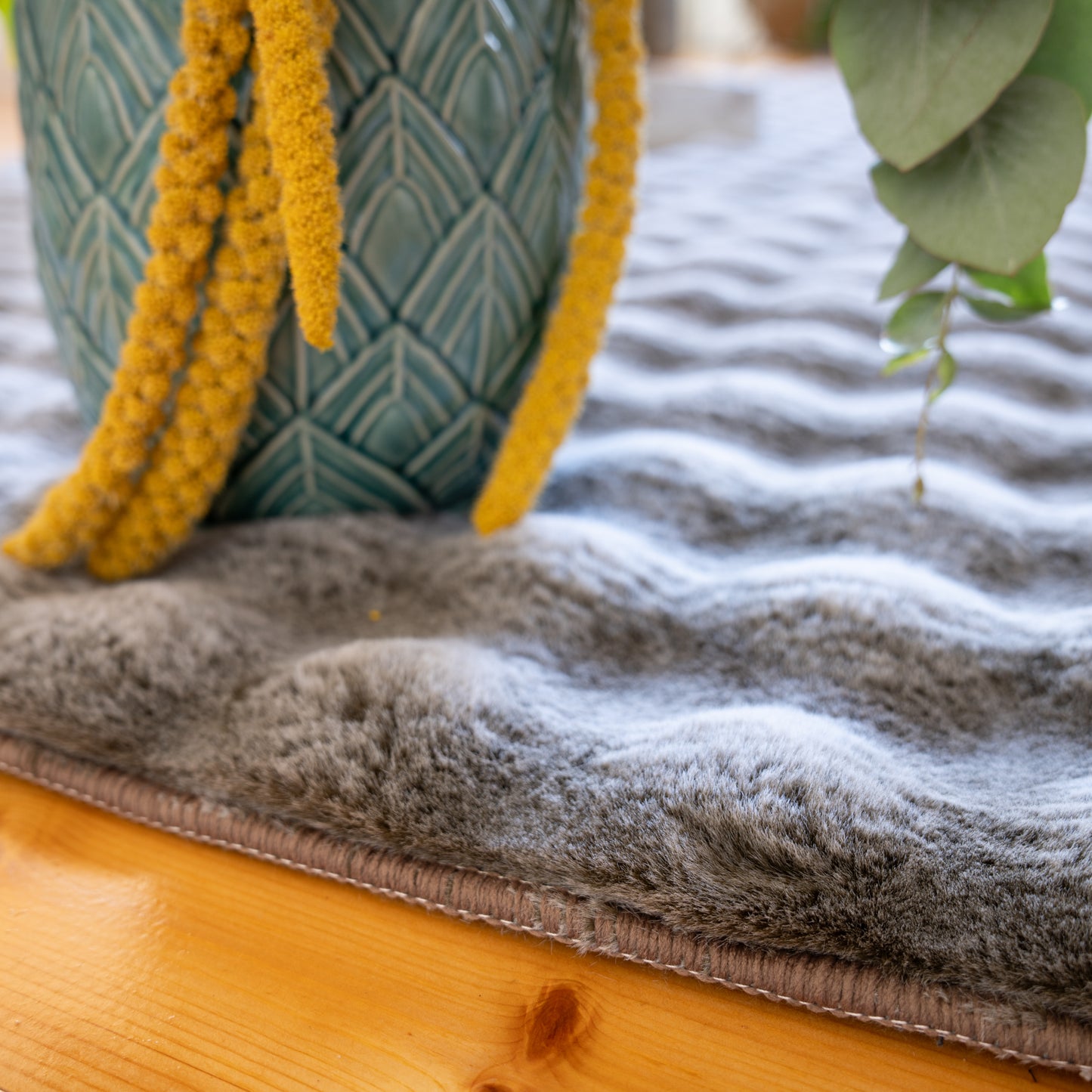 Detail van de textuur van vloerkleed My Calypso in taupe met vaas – zachte pool en hoogwaardig afgewerkt randdetail